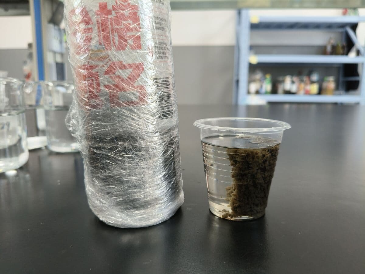 Paper mill water sample before polymer addition in a bench jar test, showing suspended fibre and filler
